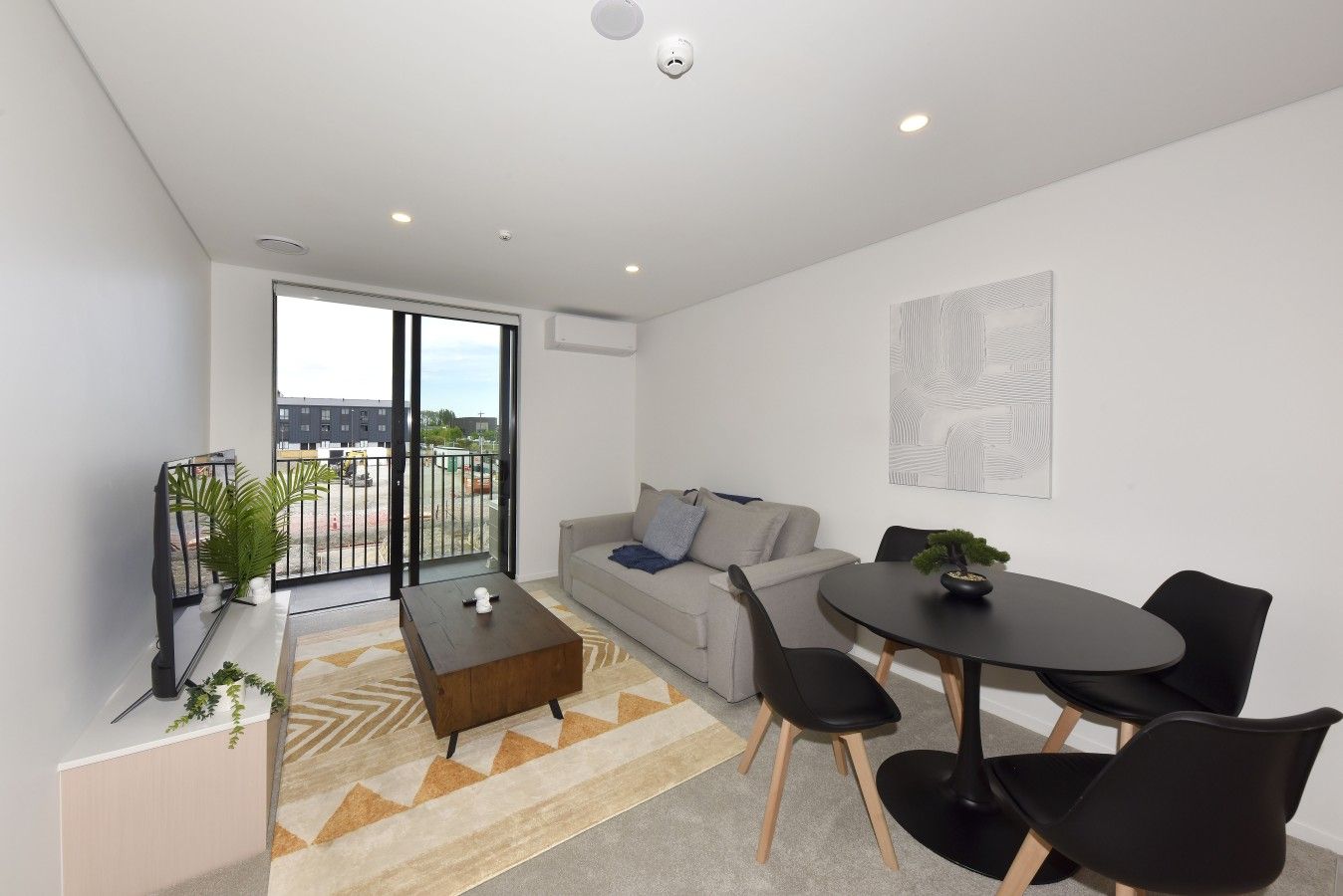 Un salon moderne comprenant un canapé, une table basse et une table à manger avec des chaises. Une porte-fenêtre coulissante donne accès à un balcon.