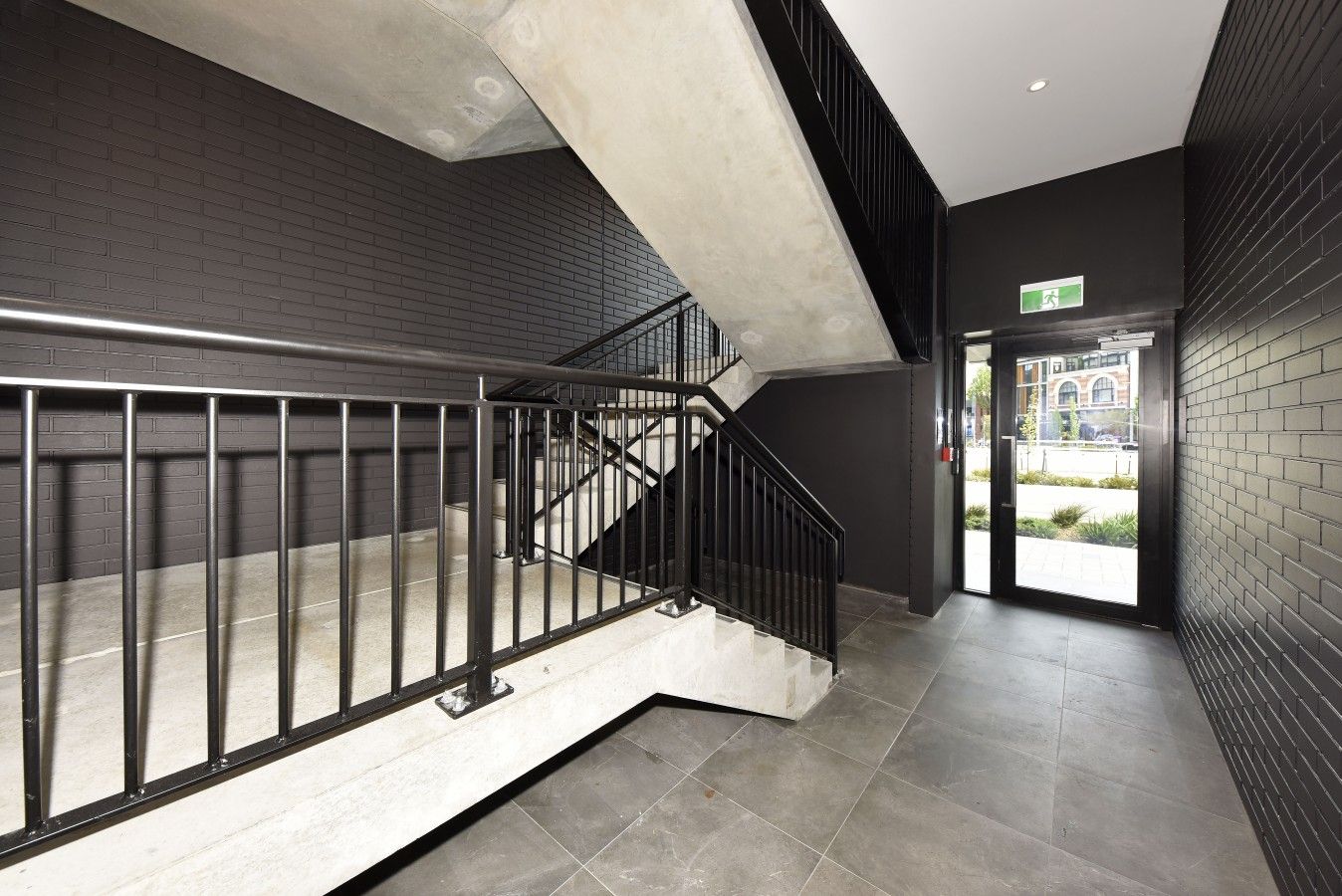 A modern staircase with metal railings, a black brick wall, and a glass door leading outside.