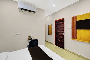 A hotel room with a bed, an air conditioner, a small table with a kettle, a chair, and a wooden door. - Townhouse Suchitra IDA Jeedimetla (Hyderabad)