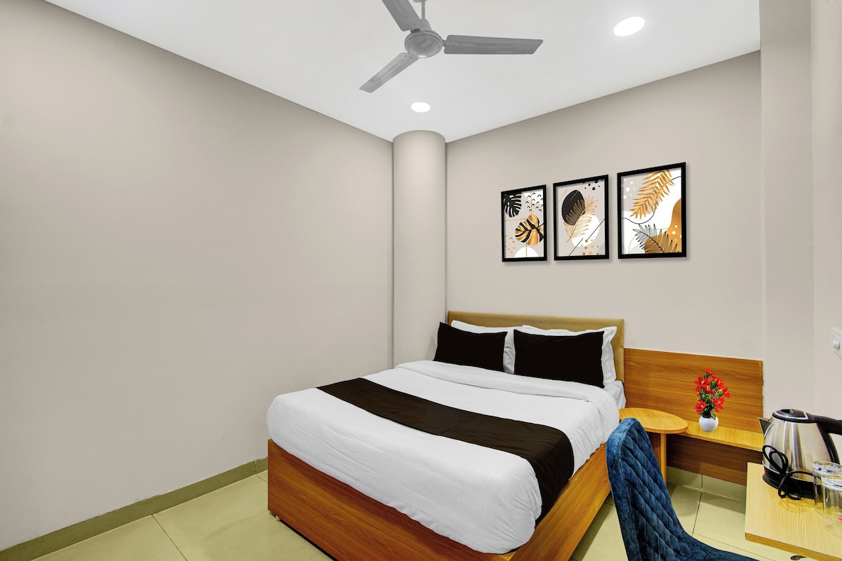 Una habitación de hotel con una cama, una mesita de noche con una lámpara, una cafetera y una obra de arte enmarcada en la pared.