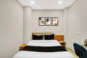 Habitación de hotel con cama, mesita de noche, una silla y tres cuadros en la pared.