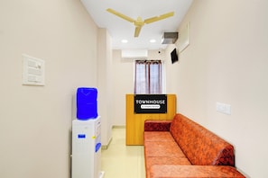 A reception area with a sofa, a water dispenser, an air conditioning unit, a ceiling fan, and a sign indicating the property is company-serviced. - Townhouse Suchitra IDA Jeedimetla (Hyderabad)