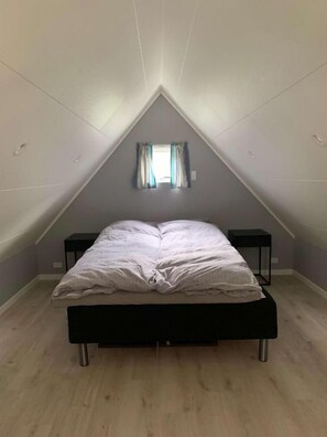 A bedroom with a sloped ceiling, a bed, two bedside tables, and a window with curtains.