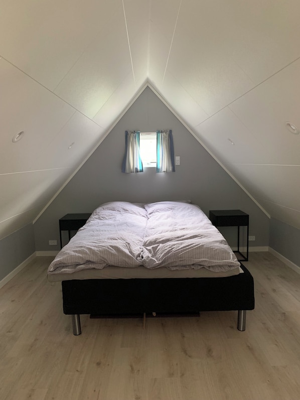 A bedroom with a sloped ceiling, a bed, two bedside tables, and a window with curtains.