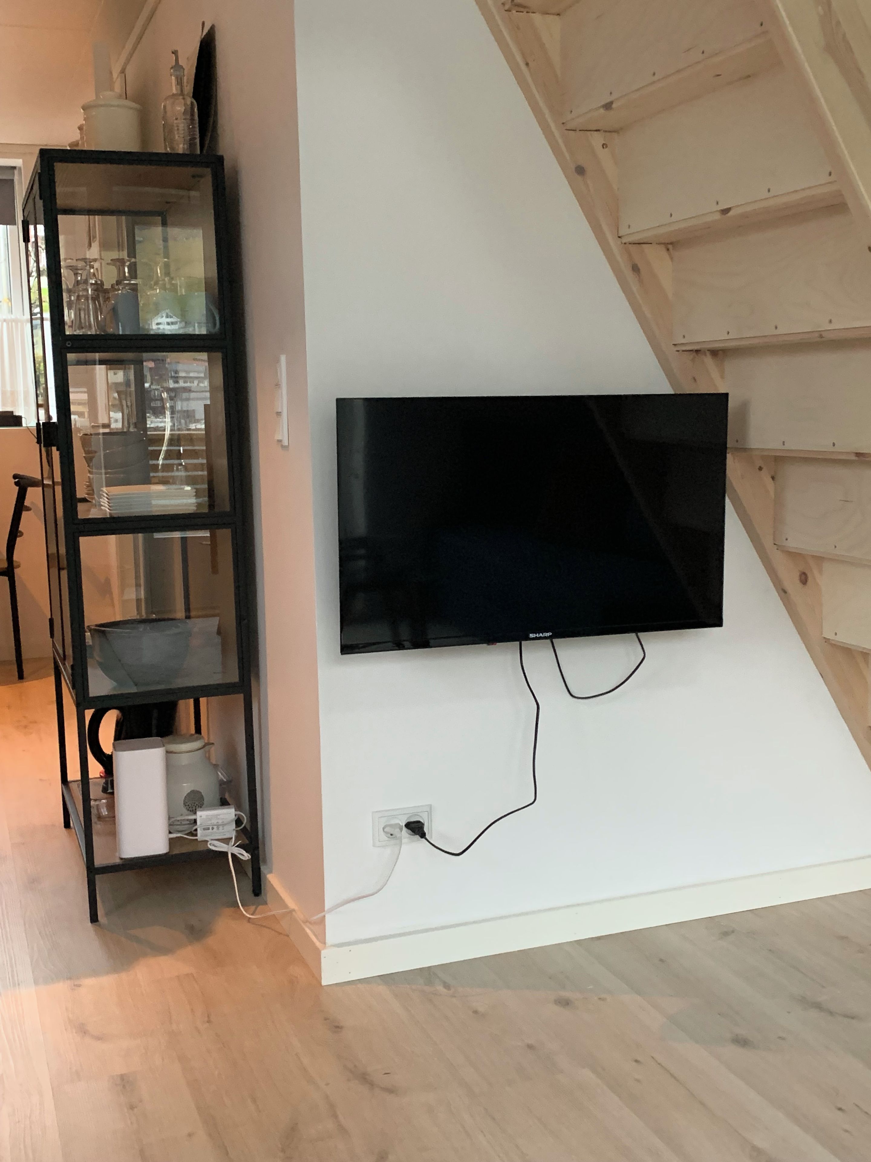 Un televisor de pantalla plana montado en una pared blanca, un mueble negro con puertas de cristal y una escalera de madera.