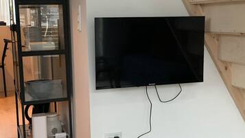 Un televisor de pantalla plana montado en una pared blanca, un mueble negro con puertas de cristal y una escalera de madera.