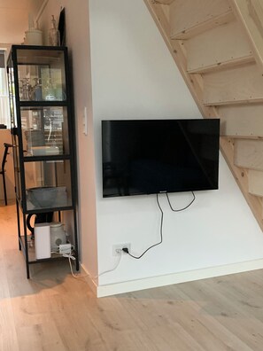 A flat-screen TV mounted on a white wall, a black shelving unit with glass doors, and a wooden staircase.