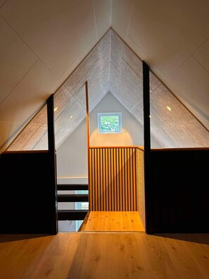 A sloped ceiling with a framed picture, wooden paneling, and a staircase leading to an upper level.