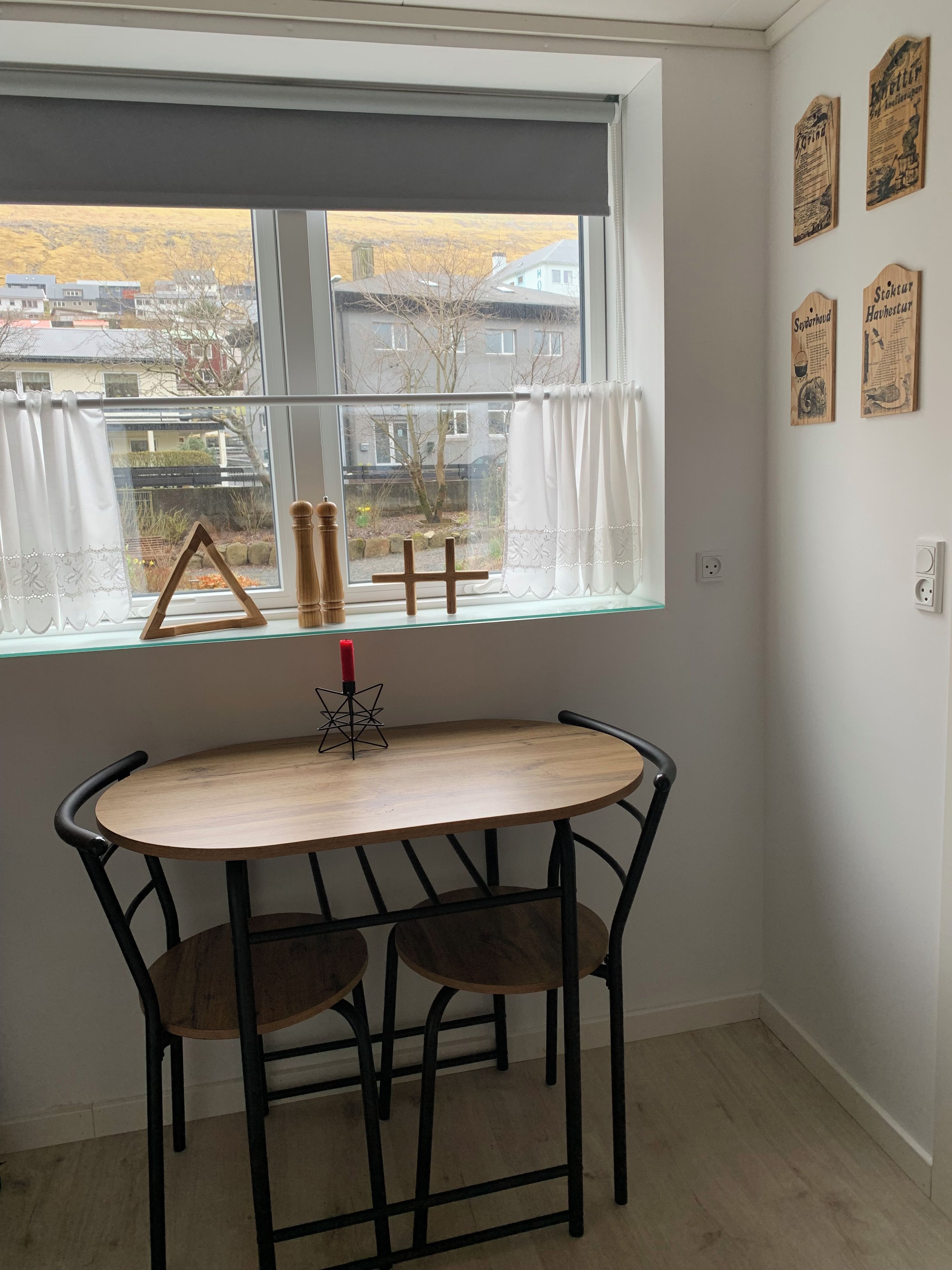 A room with a table and two chairs, a window with curtains, and wall decorations.