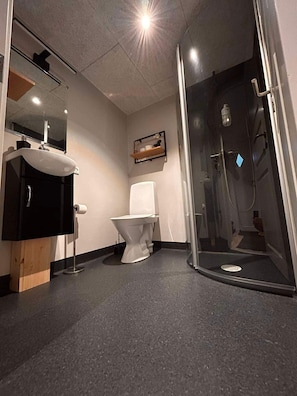 Un baño con inodoro, lavamanos y cabina de ducha con mampara de vidrio.