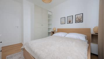 A bedroom with a bed, a wardrobe, a bedside table, and a wall with three framed pictures.