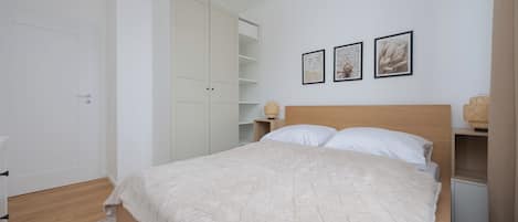 A bedroom with a bed, a wardrobe, a bedside table, and a wall with three framed pictures.