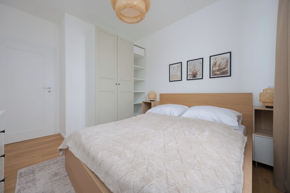 A bedroom with a bed, a wardrobe, a bedside table, and a wall with three framed pictures.