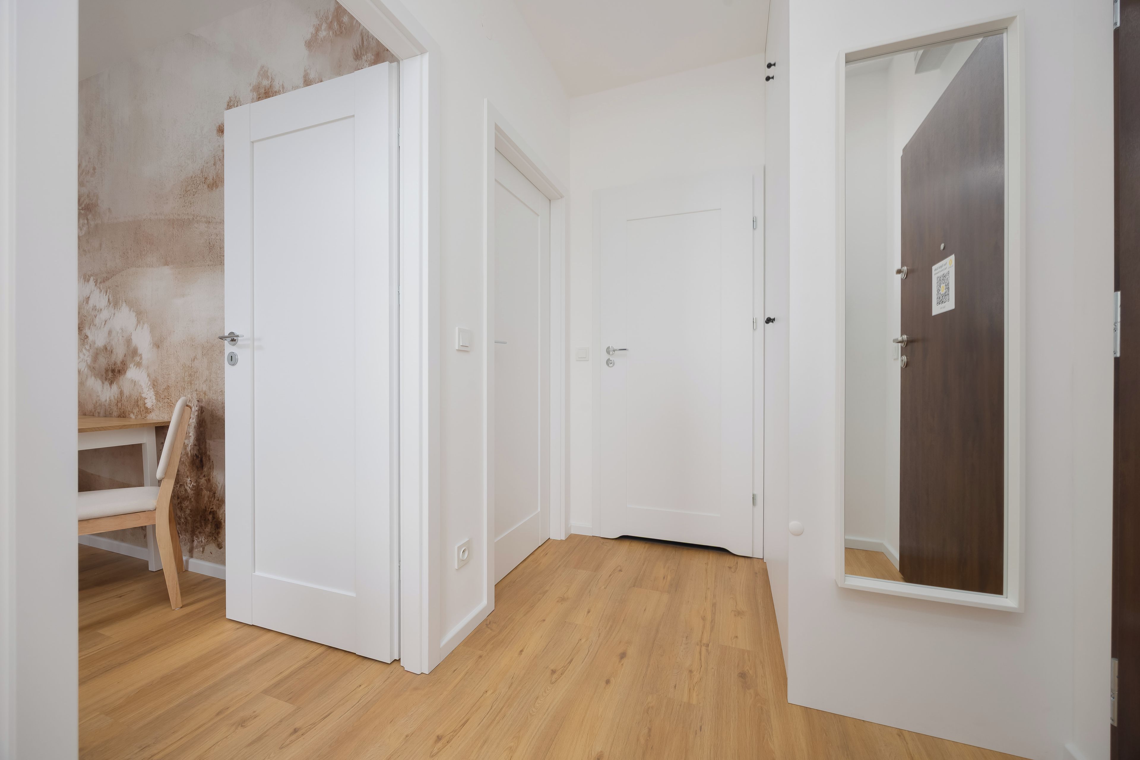A room with wooden flooring, white walls, and a door with a QR code.