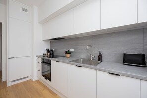 A modern kitchen with white cabinetry, a grey countertop, a stainless steel sink, and a black toaster.