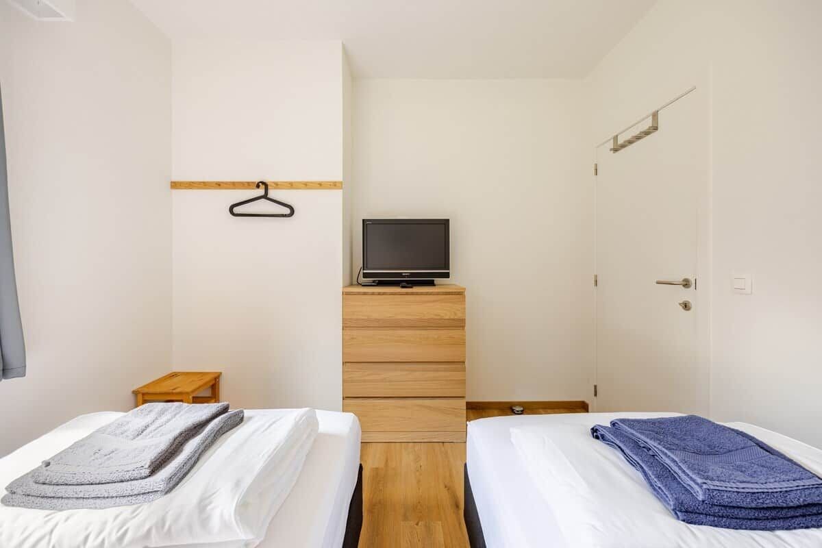 Ein Hotelzimmer mit zwei Betten, einem Fernseher auf einer Kommode, einem Holzboden und einer Tür mit Griff.