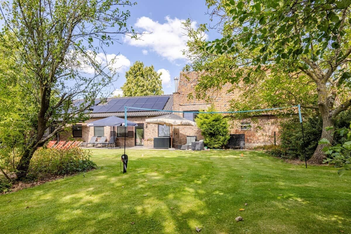 A house with a solar panel roof, a well-maintained lawn, and a patio area with outdoor furniture.