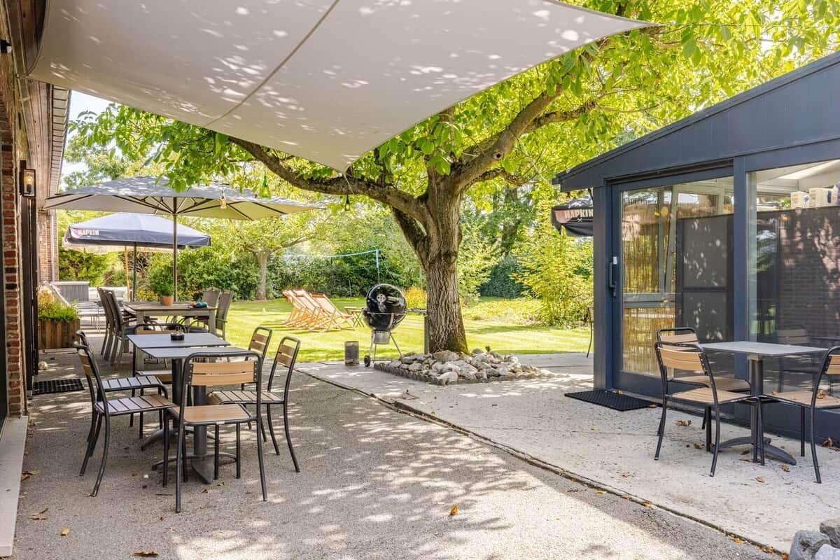 Een terras buiten met tafels en stoelen, een barbecue en parasols voor schaduw.