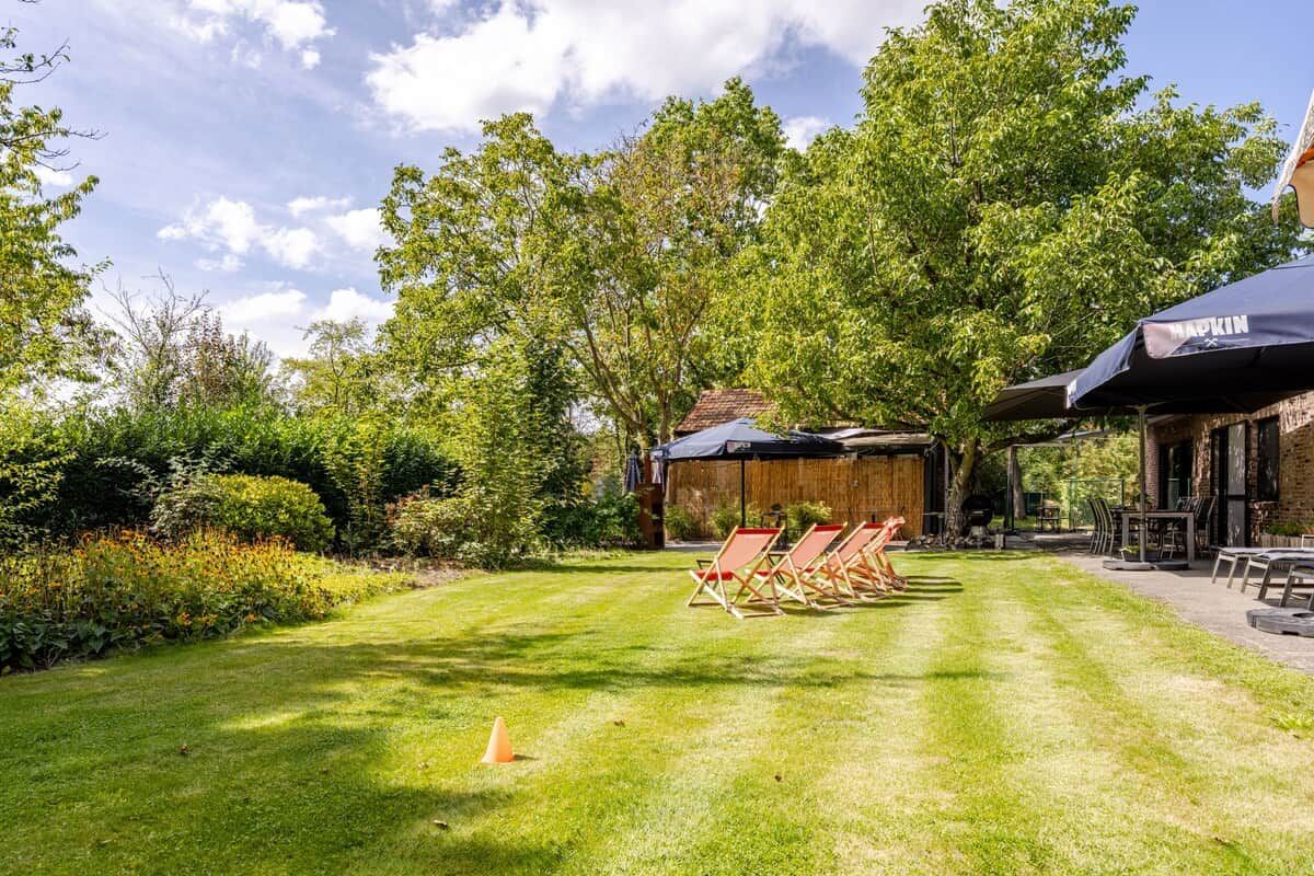Een verzorgd buitengebied met een gazon, een barbecueplaats en een zithoek met parasols.