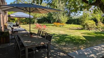 Un patio exterior con mesa y sillas, una parrilla y un gran paraguas que da sombra.