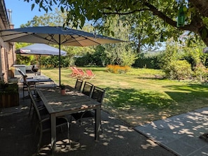 Une terrasse extérieure avec une table et des chaises, un barbecue et un grand parasol pour faire de l’ombre.