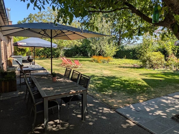 An outdoor patio with a table and chairs, a barbecue grill, and a large umbrella providing shade.