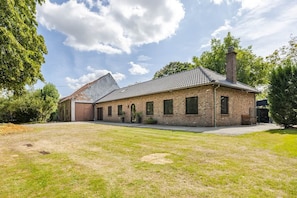 A brick building with a flat roof and a chimney, surrounded by a grassy yard and trees.
