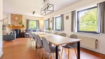 Un salon moderne avec une cheminée, un coin repas avec une longue table et des chaises, et de grandes fenêtres avec des rideaux.