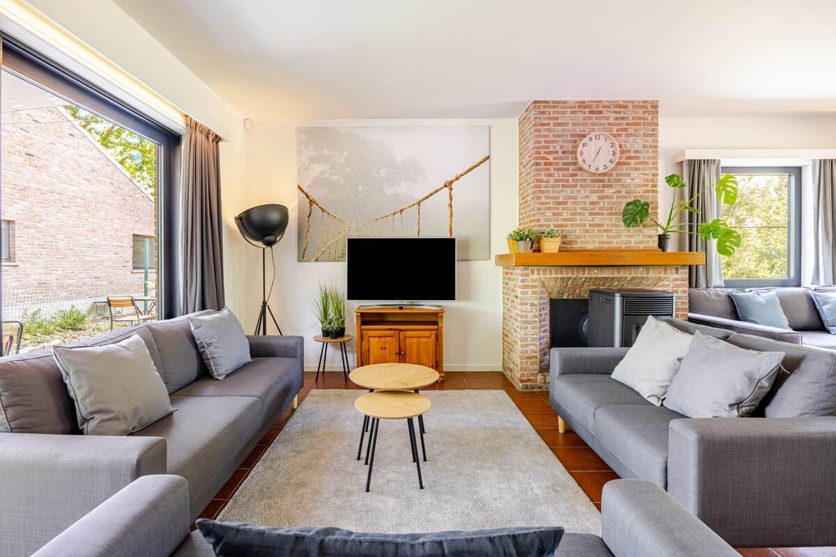 A modern living room with a fireplace, grey sofas, a flat-screen TV, and a large window.