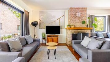 A modern living room with a fireplace, grey sofas, a flat-screen TV, and a large window.