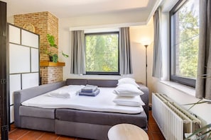 A bedroom with a bed, a brick wall, a window with curtains, a radiator, and a plant.