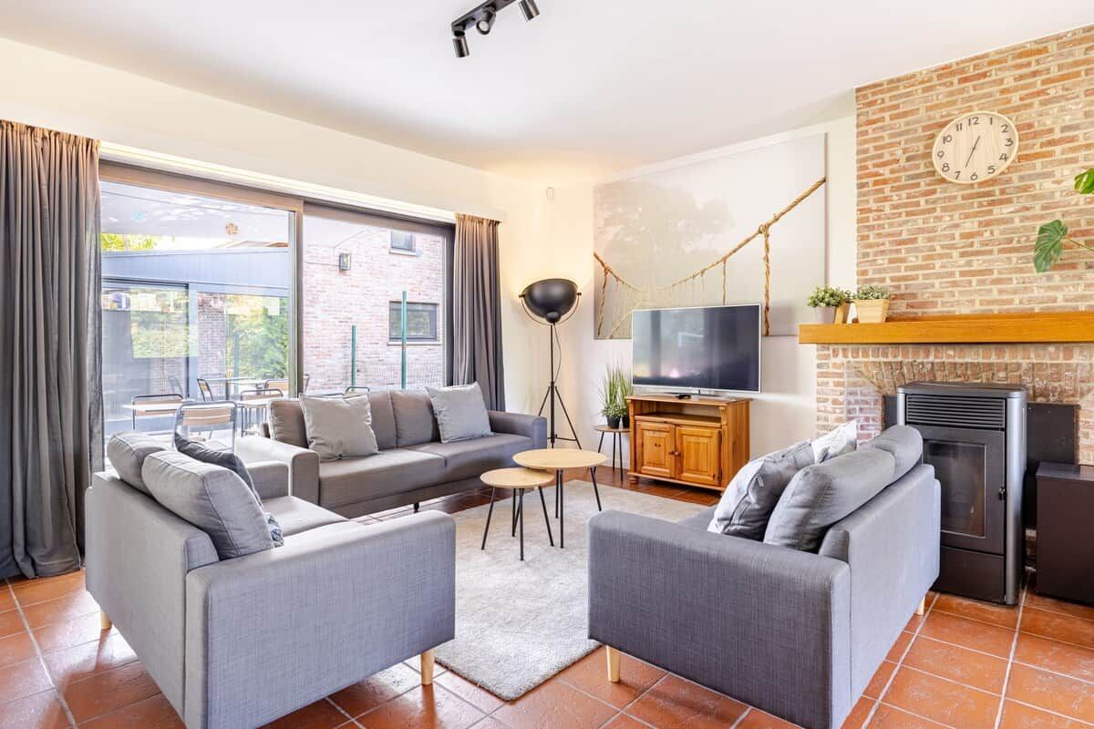 A modern living room with a sectional sofa, a TV, a fireplace, and a brick wall.