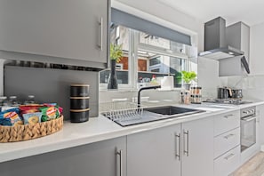 A modern kitchen with a large window, stainless steel appliances, and a variety of kitchenware. - Jameson House / 3BR/ Sleeps 7 / Free Parking (Wolverhampton)