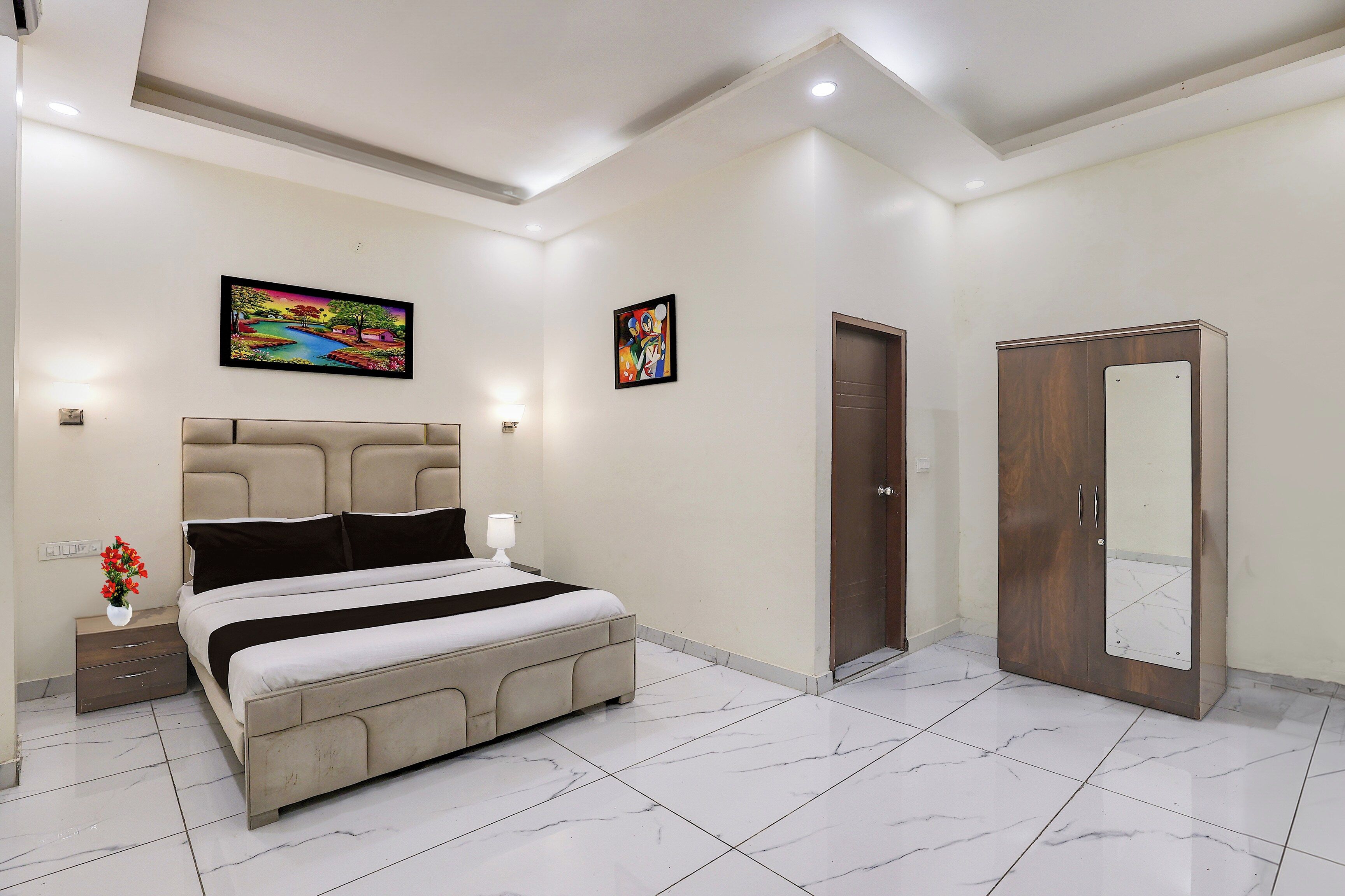 Un dormitorio con cama, mesitas de noche, un armario y dos cuadros colgados en la pared.