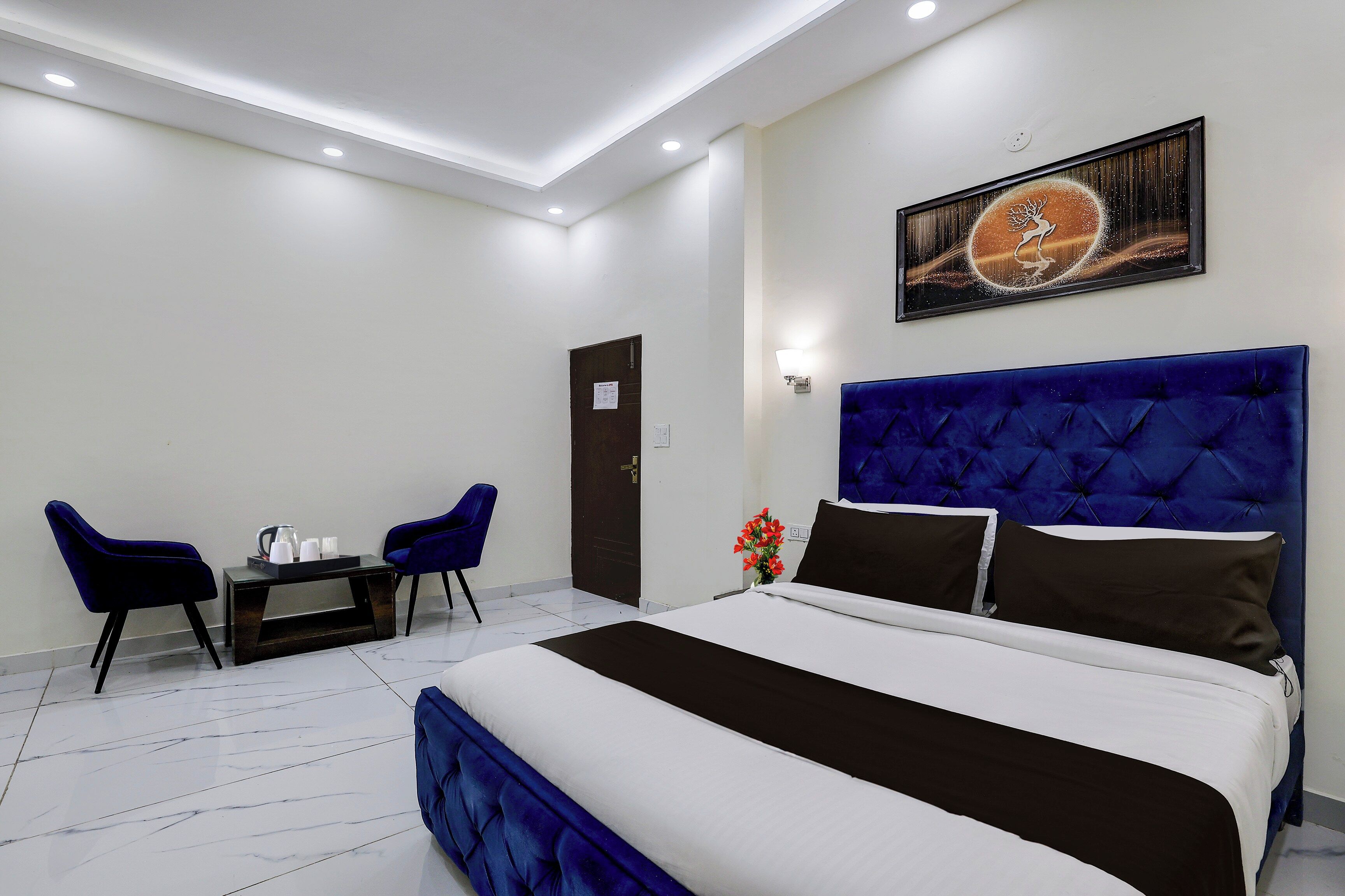 Habitación de hotel con una cama grande, un escritorio con sillas, un cuadro en la pared y una puerta.