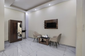 A hotel room with a wooden wardrobe, a small table with a tray of cups, two chairs, a flat-screen TV mounted on the wall, and a tiled floor. - Super Hotel O Clock Tower Dehradun (Dehradun)