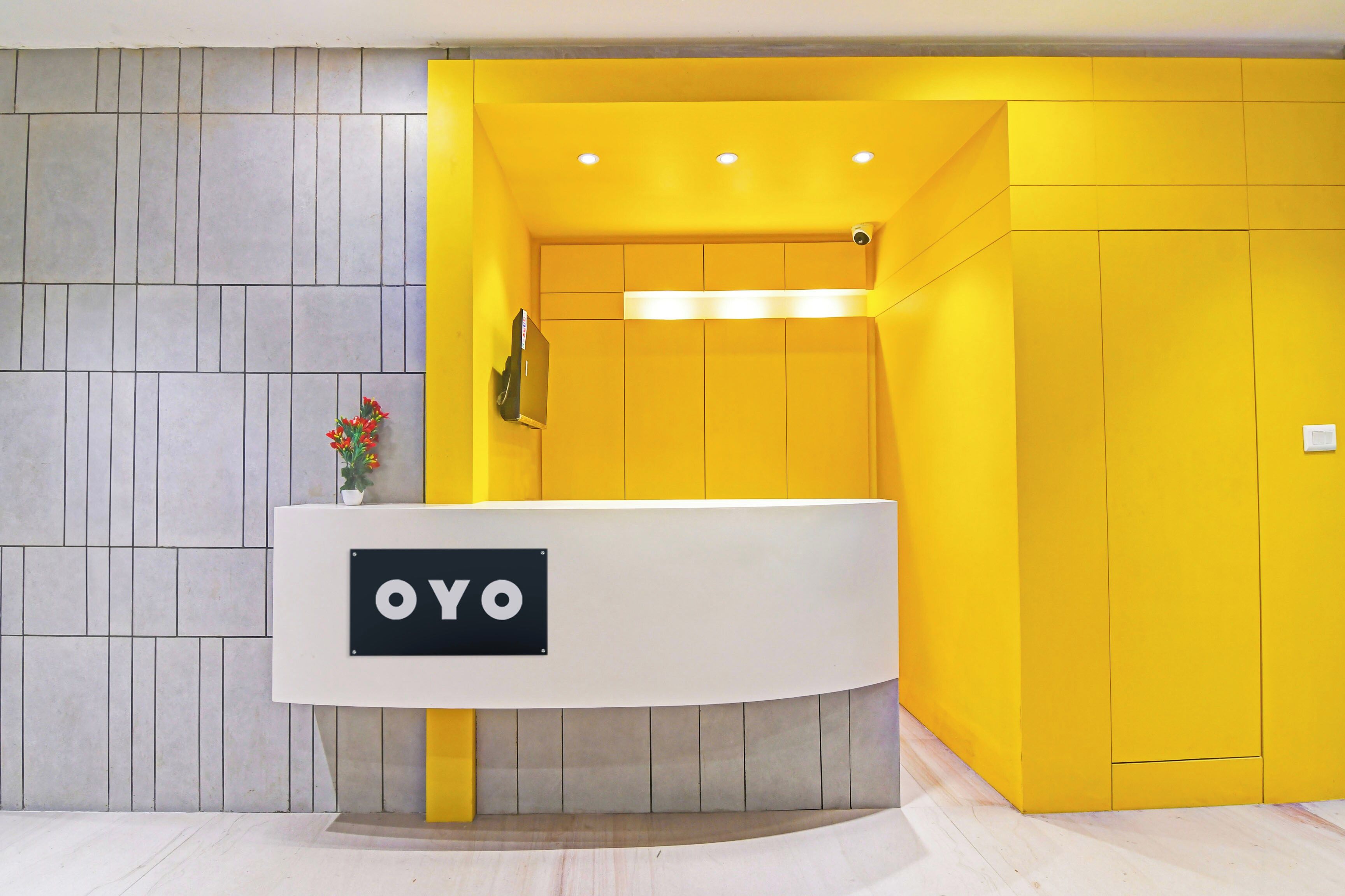 En receptionsdisk med en skylt som visar texten ”OYO” i en modern interiör med en gul accentvägg och ett grått klinkergolv.