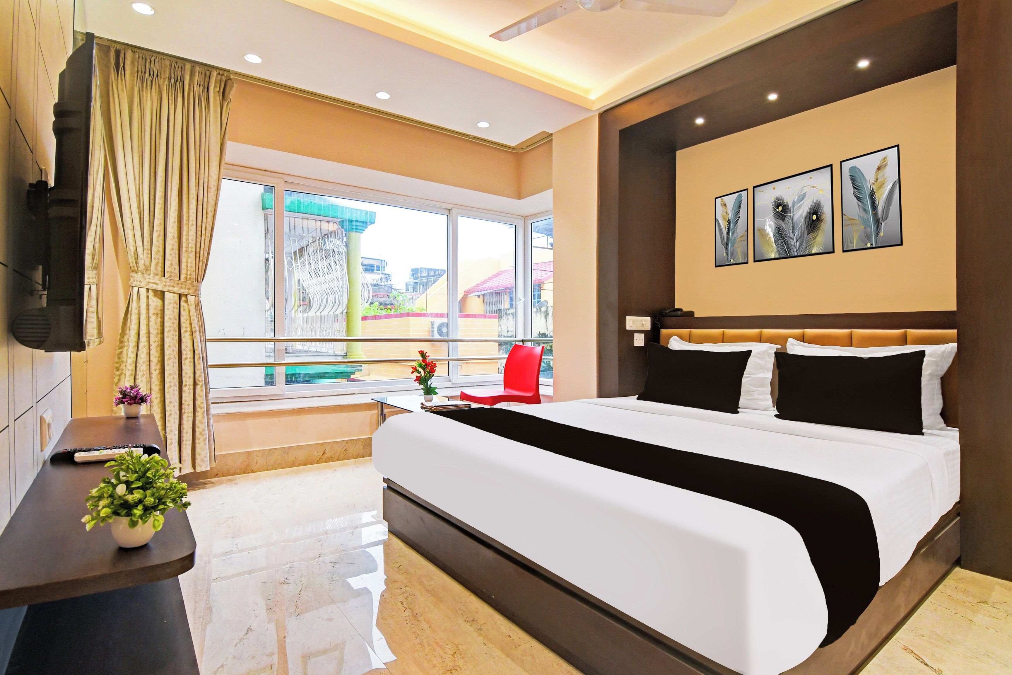 A hotel room with a large bed, a TV, a window with curtains, a red chair, and artwork on the wall.