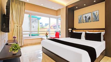 A hotel room with a large bed, a TV, a window with curtains, a red chair, and artwork on the wall.