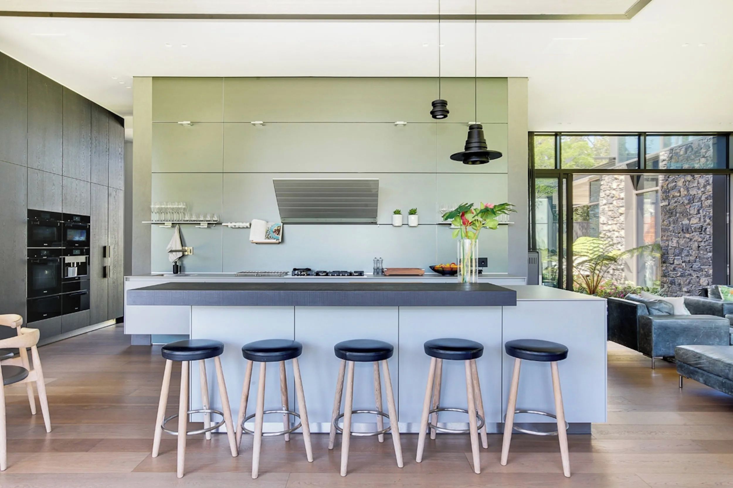 A modern kitchen with a central island, bar stools, and a dining area with a sofa.