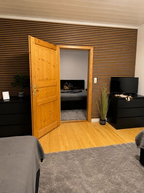 A room with a wooden door, a bed, a TV, a dresser, and a plant.