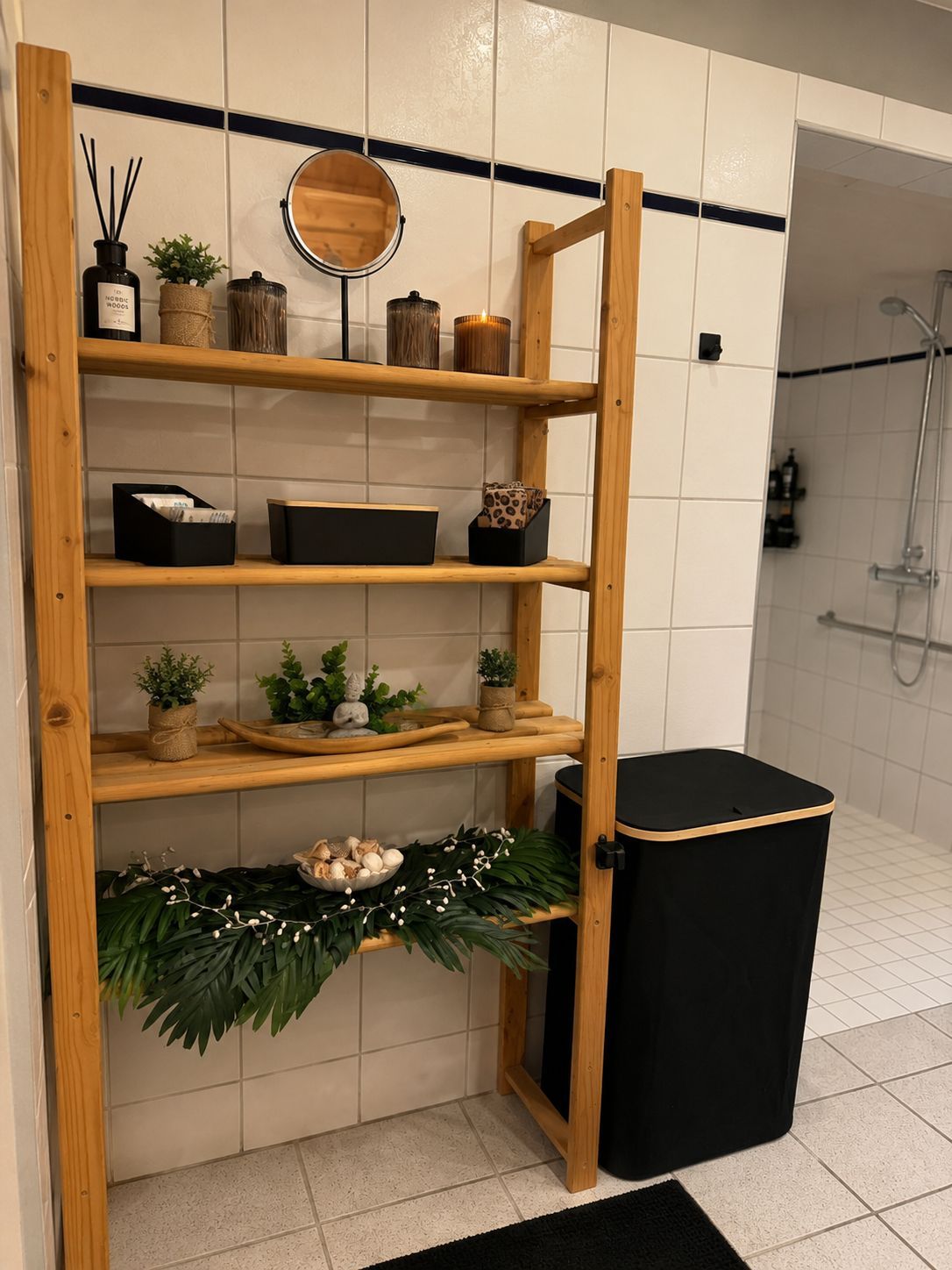 Een badkamer met een houten schapunit, een spiegel en een zwarte prullenbak.