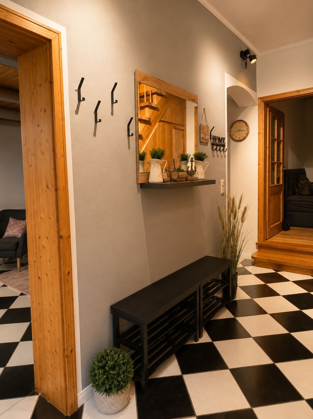 A hallway with a black and white checkered floor, a wooden bench, a mirror with a shelf above it, and a clock on the wall.