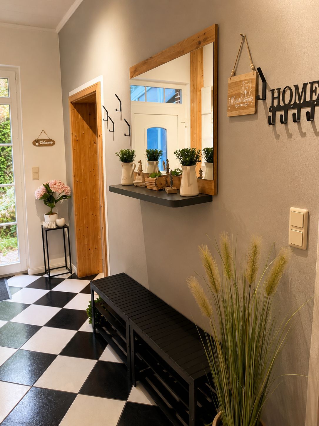 A hallway with a black and white checkered floor, a wooden bench, a mirror with a hanging sign, and a wall-mounted light switch.