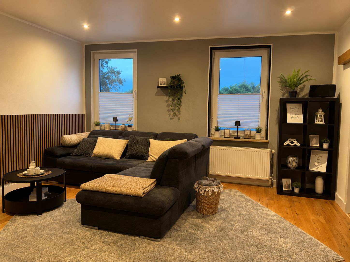 A living room with a dark-colored sofa, a small side table, a floor lamp, and a bookshelf.