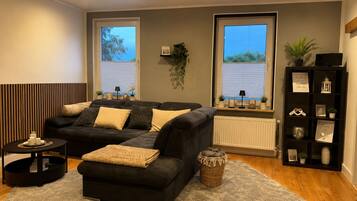 A living room with a dark-colored sofa, a small side table, a floor lamp, and a bookshelf.