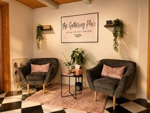 A cozy room with two armchairs, a small table, a framed sign, and hanging plants.