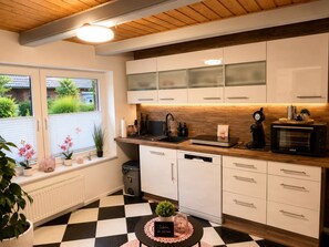 A modern kitchen with white cabinets, a black and white checkered floor, and a window with a view of greenery.