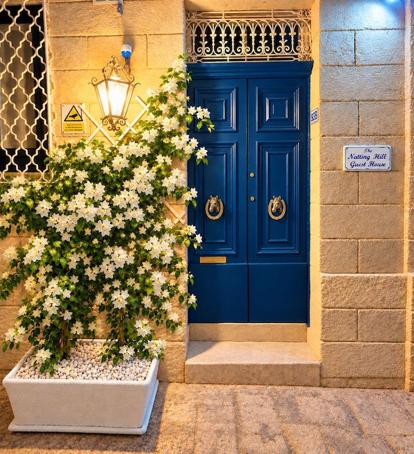 A blue door with a sign above it, a potted plant with white flowers, and a warning sign on the wall. - The advantages of a detached house with services and quality of a boutique hotel (Il-Belt Valletta)