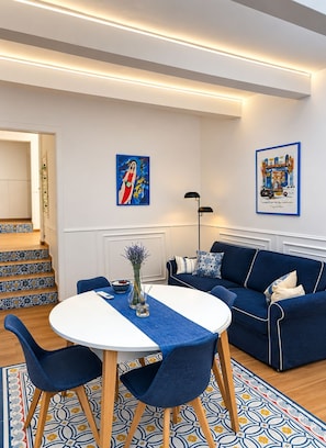 A modern living room with a blue sofa, a round table, and a staircase with patterned tiles. - The advantages of a detached house with services and quality of a boutique hotel (Il-Belt Valletta)